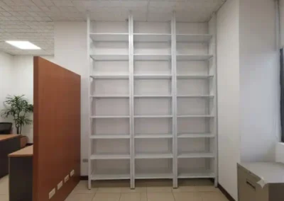 Estantería industrial metálica de tres cuerpos en color blanco con repisas perforadas de altura regulable, instalada en una oficina corporativa.